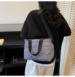 Side view of gray quilted tote bag with bow embroidery and black wide shoulder strap