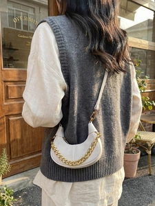 Elegant white half-moon crossbody bag with gold chain strap in a stylish street setting