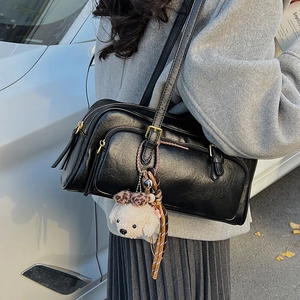 Close-up of black retro boston bag featuring a plush teddy bear charm and metal zipper details