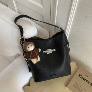 Detail of black litchi grain leather bucket bag with silver lock and bear charm
