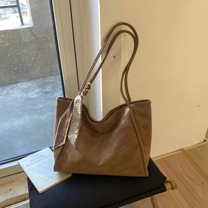 Detail of a brown suede tote bag with silk scarf on a black folding stool