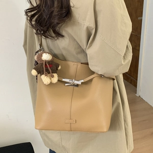 Close-up of camel leather bucket bag with metallic toggle closure and cute bear charm