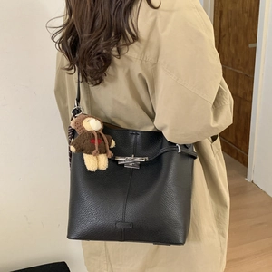 Close-up of black lychee leather bucket bag with silver turn-lock and teddy bear charm