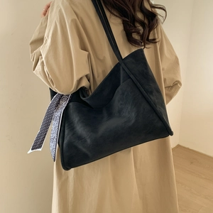 Detail of black matte leather tote bag with decorative patterned silk scarf on shoulder