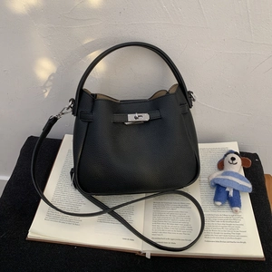 Detail of black lychee grain leather bucket bag with silver twist lock on open books