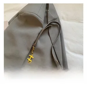 Gros plan sur un sac bandoulière en daim marron avec pendentif H doré et chaîne perlée