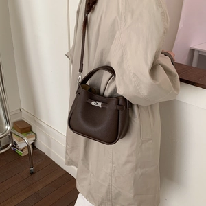 Detail of dark brown pebble leather bucket bag with silver clasp worn with a beige trench coat