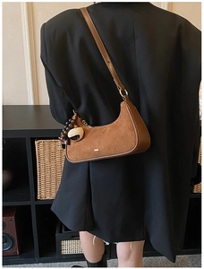 Close-up of brown suede hobo bag with leather piping and decorative wood bead charm