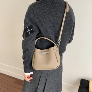 Detail of beige pebble leather bucket bag with silver metal lock and curved handle