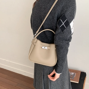 Detail of beige pebbled leather bucket bag featuring a metal twist lock and soft silhouette