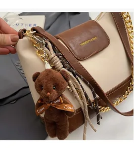 Detail of cream and brown crossbody bag with gold chain strap and teddy bear charm