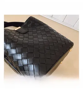 Détail du sac seau en cuir tressé noir avec des pieds de protection en métal doré sur le fond