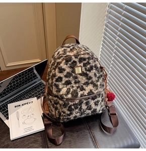 Detail of leopard print plush backpack with brown leather trim and red pompom charm