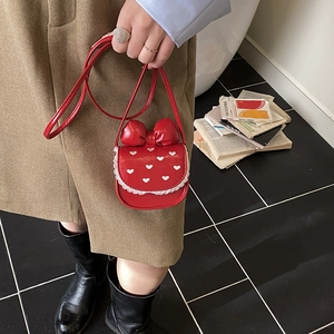 Detail view of red glossy crossbody bag featuring bow decoration and white lace trim