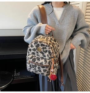 Close-up of leopard faux fur backpack with brown leather straps and red pompom charm