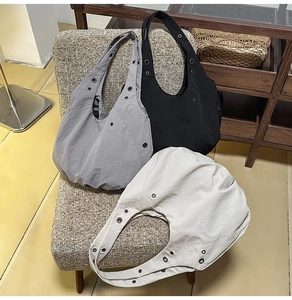 Close-up of nylon hobo bags with metal eyelets in dark grey, black, and off-white colors