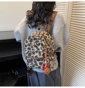 Detail shot of plush leopard print backpack with brown leather straps and fuzzy charm balls