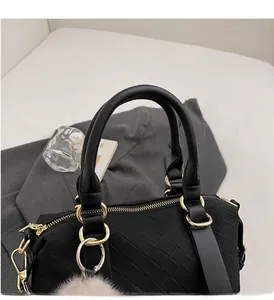 Detail of black woven baguette bag with golden hardware and gray fluffy ball charm