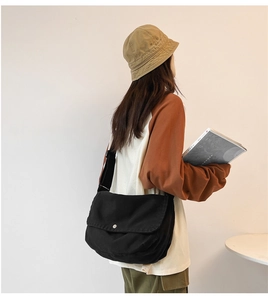 Detail of adjustable strap and silver snap button on large black canvas messenger bag