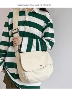 Detailed close-up of cream canvas messenger bag with metal button on striped polo outfit