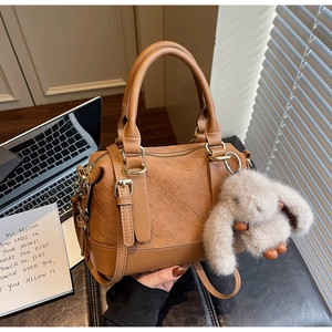 Braune geflochtene Boston-Tasche mit Plüschhasen-Anhänger neben Laptop und Notizen