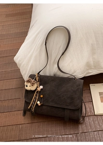 Close-up of retro dark grey messenger bag with plush bear charm on white pillow