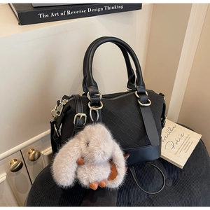 Detail of black woven texture handbag with grey plush bunny charm and gold hardware