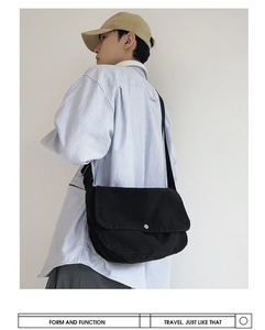 Detailed view of black canvas messenger bag worn by male model in stripes