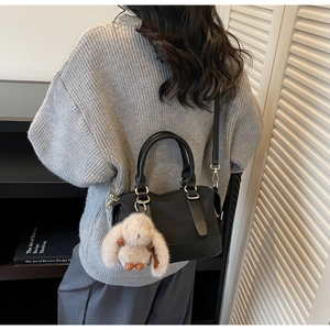 Details einer schwarzen Handtasche mit Webstruktur, Hasenanhänger und Schultergurt
