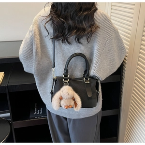 Detail of black quilted baguette bag with gold hardware and plush bunny charm on a model
