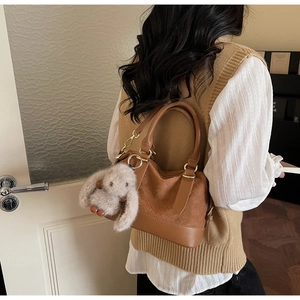 Brown woven texture handbag with plush rabbit accessory on a model in a modern interior