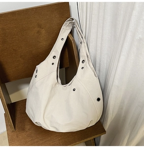 Detail of off-white oversized canvas tote bag with black metal eyelets hanging on a chair