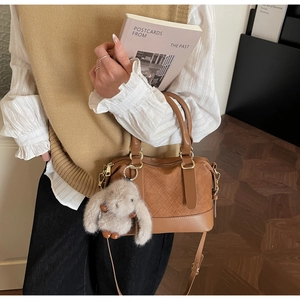 Details der karamellbraunen Boston-Tasche mit Webstruktur und süßem Kaninchen-Anhänger