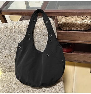 Detailed close-up of black nylon hobo bag with silver metallic rivets on the shoulder strap