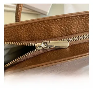 Detail of silver zipper closure and brown lychee grain leather texture on the bucket bag