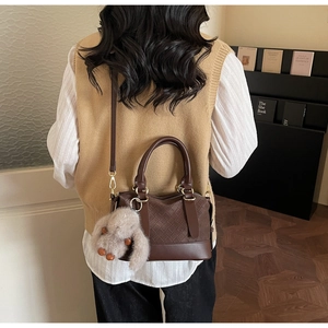 Detailansicht der braunen geflochtenen Ledertasche mit Plüschhasen-Anhänger und rundem Griff