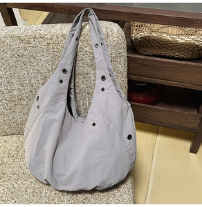 Detail of grey nylon tote bag with metal eyelets on a woven sofa in a lifestyle setting