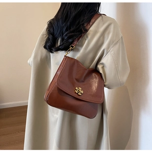 Detail of a brown leather shoulder bag with a gold flower buckle on a beige trench coat