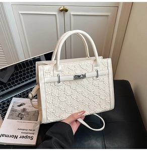 Detail of a creamy white textured handbag featuring a silver turn-lock and leather straps