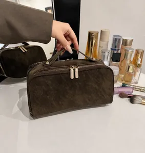 Detailansicht der braunen Wildleder-Kulturtasche mit goldenen Reißverschlüssen
