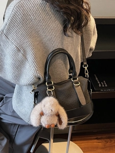 Schwarze Boston-Tasche mit gewebter Textur und Plüschhasen-Anhänger von Model getragen