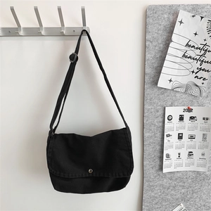 Detail of black canvas messenger bag with adjustable strap and metal button on white wall