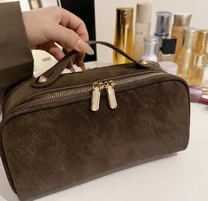 Detail einer braunen Wildleder-Kosmetiktasche mit goldenen Reißverschlüssen und Tragegriff
