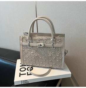 Close-up of beige pleated textured Kelly bag with silver metal lock on a book