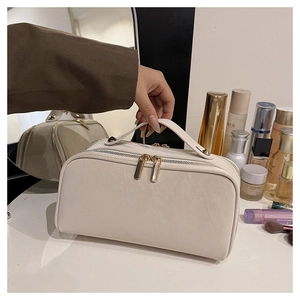 Gros plan d'une trousse de toilette en cuir crème avec fermetures éclair dorées