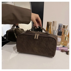 Détail d'une trousse de maquillage en daim marron avec double fermeture dorée et poignée