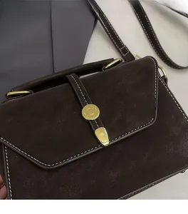Detail of dark brown leather crossbody bag with white contrast stitching and gold lock