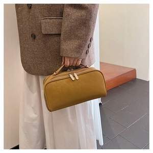 Trousse de toilette jaune gingembre tenue par un mannequin en tenue de blazer élégante