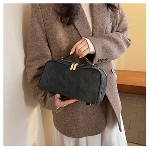 Détail de la trousse de toilette en cuir noir avec zips dorés et poignée solide