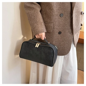 Détail d'une trousse de toilette en cuir noir mat avec doubles fermetures éclair dorées et anses